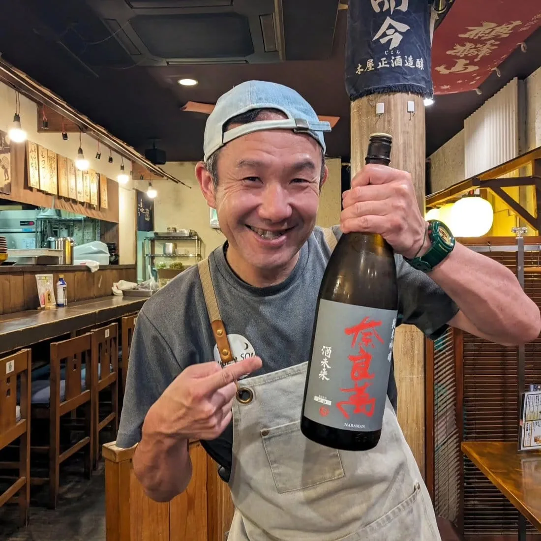 藤枝市場の店内で、日本酒の瓶を持って笑う店主